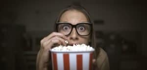 This is a picture of funny scared woman watching horror movies and eating popcorn at home for an article called Why Competitive Intelligence can help any size company by Octopus Competitive Intelligence who answer the questions when you just need to know