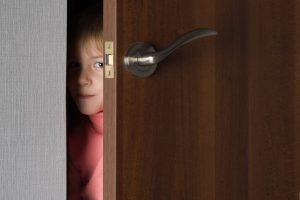 This is a picture of A child, a little girl, looks out from the ajar door of the room for an article called Exploit Your Competitive Intelligence Discoveries by Octopus Competitive Intelligence Competitor Analysis