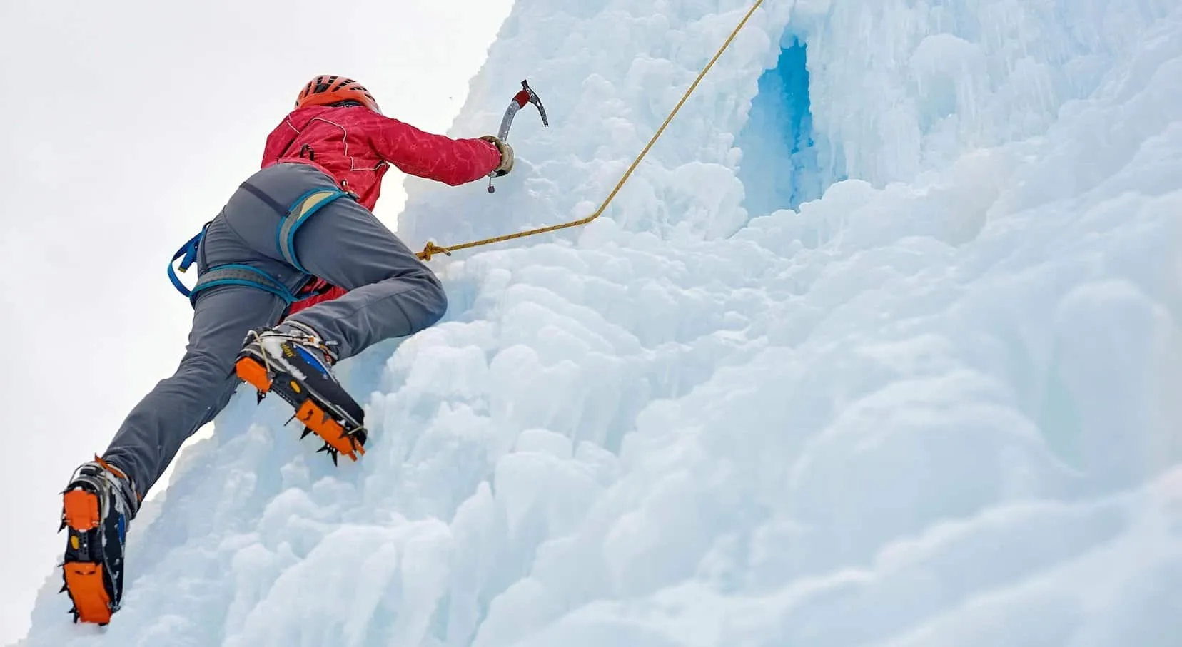 This is a picture of an Alpinist woman with ice tools axe in orange helmet climbing a large wall of ice for an article called Which industries use Competitive Intelligence and why? By Octopus Competitive Intelligence company. We answer the questions with Competitive Intelligence, Due Diligence and business development