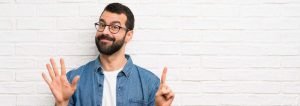 This is a picture of a man with beard over white brick wall counting six with fingers for an article called 6 reasons when Competitive Intelligence is essential by Octopus Intelligence and Corporate Investigations get in touch no obligation chat