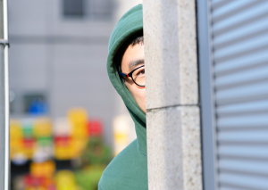 This is an image of a man in a green hoodie looking around a corner for an article called How to Identify Your Competitors and to understand them better by octopus competitive intelligence agency market intelligence company and counterintelligence solutions