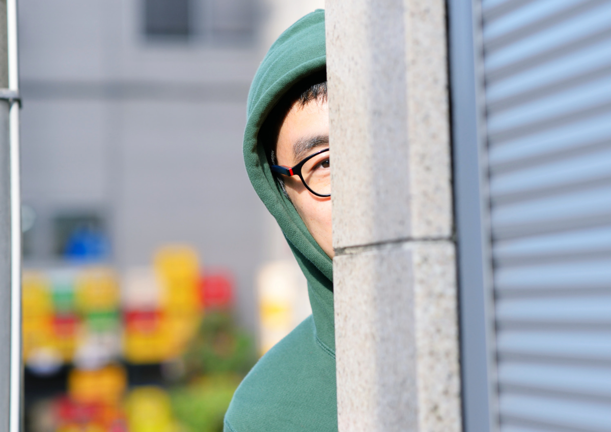 This is an image of a man in a green hoodie looking around a corner for an article called How to Identify Your Competitors and to understand them better by octopus competitive intelligence agency market intelligence company and counterintelligence solutions